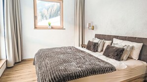 Une chambre à coucher avec un lit, des rideaux, une fenêtre donnant sur un paysage agréable et une lampe fixée au mur.