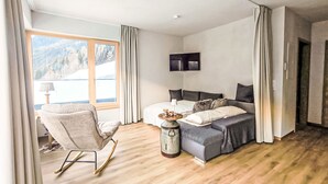 Une chambre avec un lit, une chaise, une télévision et une fenêtre donnant sur la montagne.