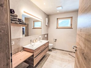 Une salle de bain moderne avec un meuble-lavabo en bois, un grand miroir, des toilettes et une fenêtre.
