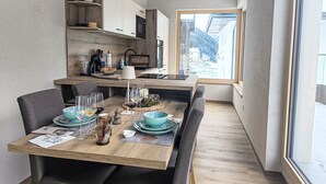 Une cuisine compacte avec des meubles en bois, un coin repas avec une table pour quatre personnes et une grande fenêtre offrant une vue sur l’extérieur.