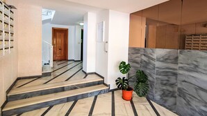 Eine Treppe mit Marmorboden, die zu einem Aufzug führt, mit einem Blumentopf und einer Wand mit strukturierter Oberfläche.