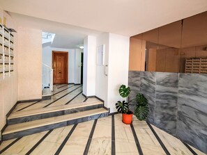 Eine Treppe mit Marmorboden, die zu einem Aufzug führt, mit einem Blumentopf und einer Wand mit strukturierter Oberfläche.
