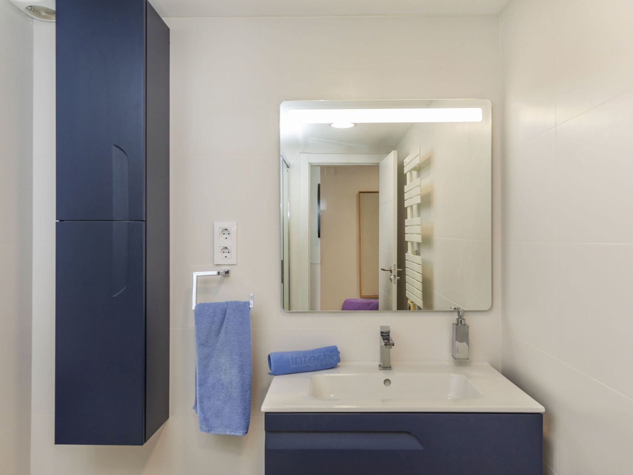 Een badkamer met een witte wastafel, een spiegel, een blauwe handdoek en een donkerblauwe kast.