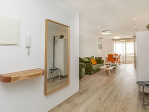 A modern living room with a green sofa, a wooden sideboard, a mirror, and a dining area with orange chairs. - Los Delfines by Interhome (Miami Platja)