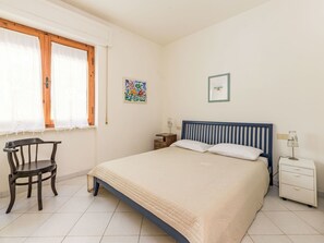 Habitació amb llit, una cadira, una tauleta de nit i una finestra amb cortines.
