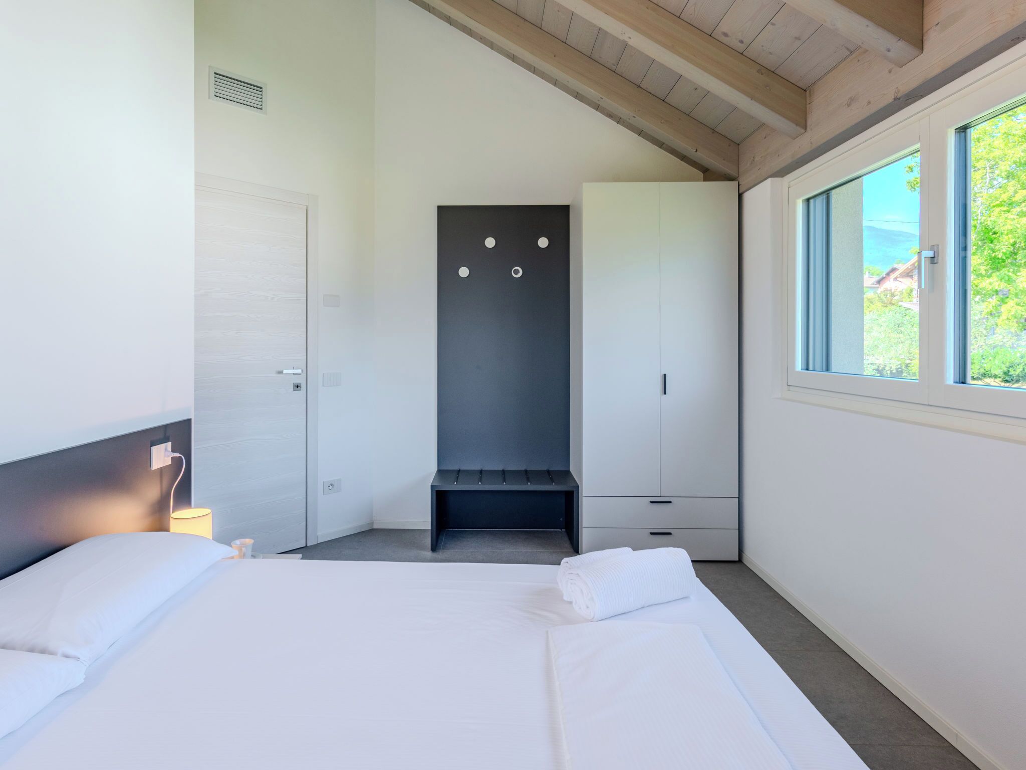 A bedroom with a bed, a wardrobe, a bench, and a window with a view.