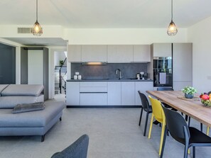 A modern kitchen with a central island, a dining area with a wooden table and chairs, and a grey sofa. - La Serena by Interhome (Colico)