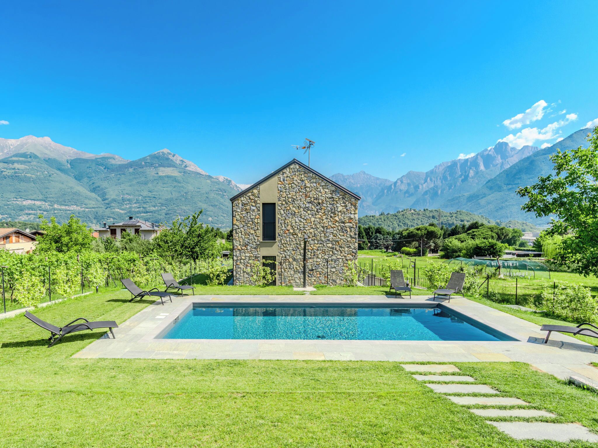 A stone building with a pool, surrounded by a well-maintained lawn and mountains in the background.