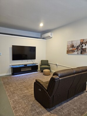 A modern living room with a flat-screen TV, a leather sofa, a green armchair, and a painting on the wall.