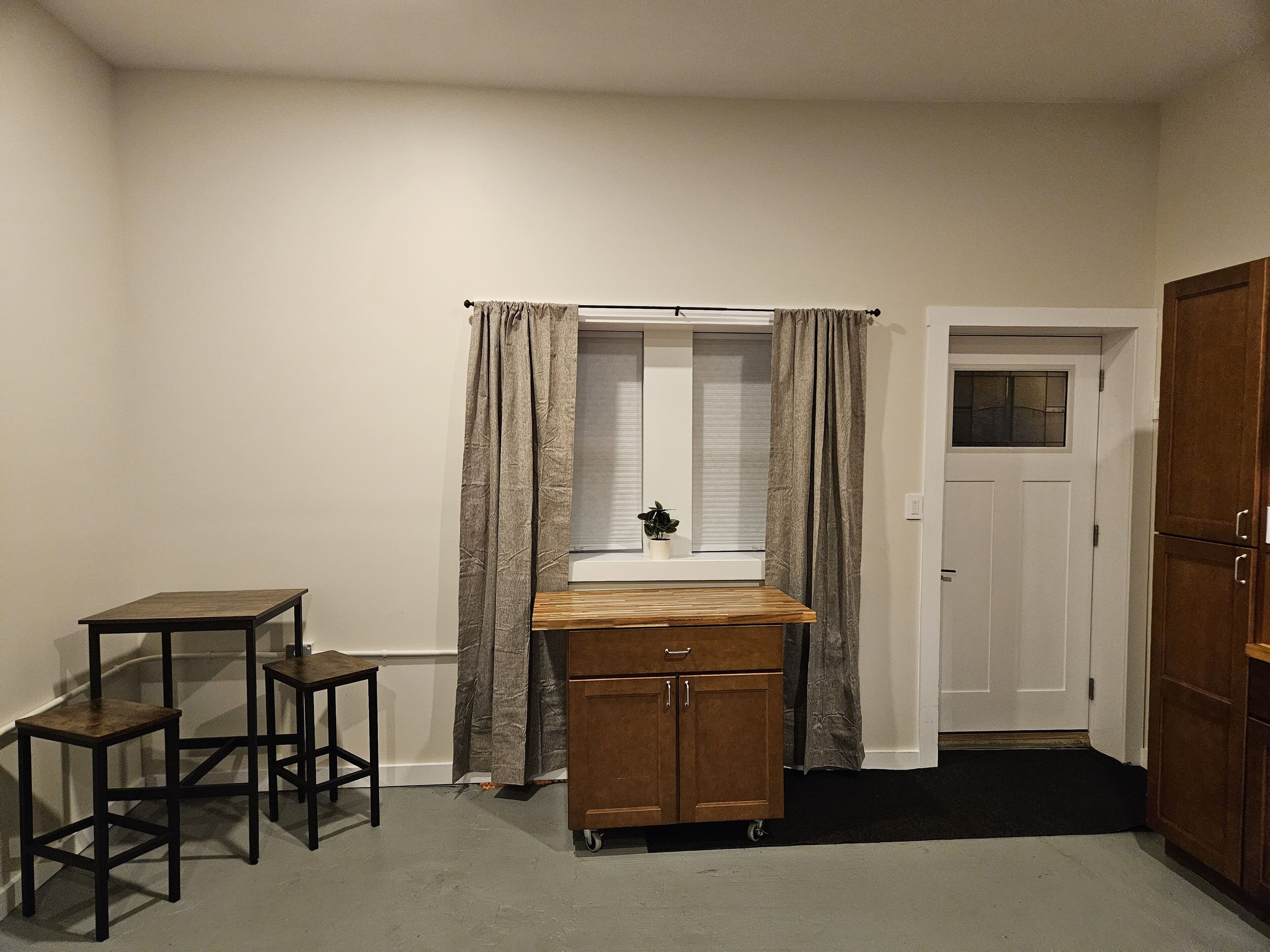 Une petite pièce avec une fenêtre, un meuble en bois, une petite table et une porte.
