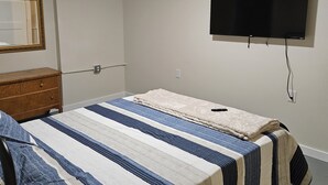 Una camera da letto con un letto, una ventola a soffitto, una TV montata a parete e un comò in legno.