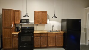 Cucina con mobili in legno, piano cottura nero, forno a microonde, lavandino e frigorifero nero.