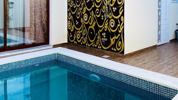 A swimming pool with a tiled edge, a glass door leading to a bathroom, and a wall with a geometric pattern. - Villa sabrina gold (Djerba Midun)
