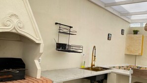 A kitchen with a brick oven, a sink, a hanging rack, and a window above the counter. - Villa sabrina gold (Djerba Midun)