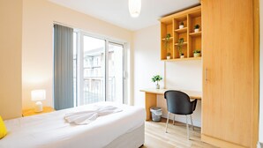A hotel room with a bed, a desk, a chair, a wardrobe, and a window with curtains. - Clean & Spacious 4 Bedroom in Limerick (Limerick)