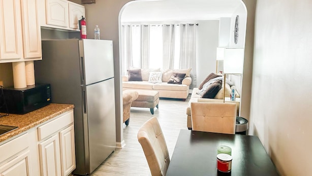 Cocina compacta con refrigerador, microondas y alacenas. Se observa una mesa de comedor con una taza.