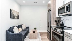 A modern living room with a grey sofa, a wooden coffee table, and a cityscape painting on the wall.