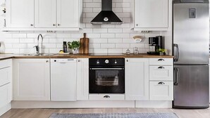Una cocina moderna con armarios blancos, una campana extractora negra, un refrigerador de acero inoxidable y un horno.