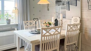 Un comedor con una mesa blanca, sillas, una lámpara colgante y una pared decorada con motivos náuticos.
