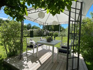 A covered outdoor patio with a table and chairs, surrounded by greenery. - 4 Star Holiday Home in Farjestaden (Farjestaden)