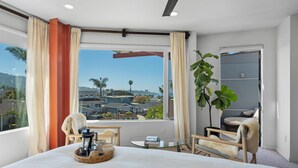Una camera d'albergo con un letto grande, un tavolino rotondo, una sedia, una pianta e vista sulla città.