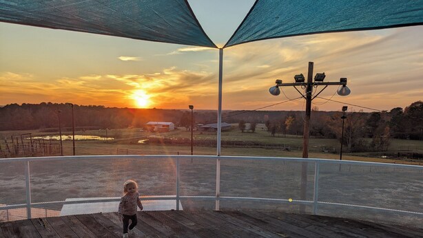 Eine Holzdielen-Terrasse mit einem Maschen-Sicherungsnetz, mit Blick auf einen Sonnenuntergang über einer ländlichen Landschaft.