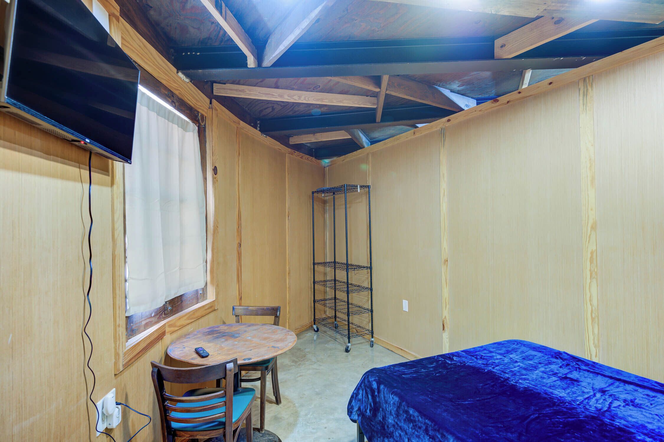 A room with a bed, a table with chairs, a window with curtains, and a metal shelf unit.