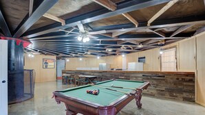 Ein Billardtisch in einem Raum mit freiliegenden Holzbalken, einer Bar und einer Lounge-Ecke.