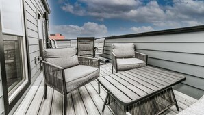 Una terrazza sul tetto con un pavimento in legno, due sedie in vimini, un piccolo tavolino rotondo e vista sul cielo e sulle nuvole.