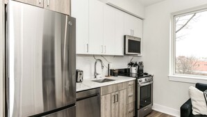 Una cucina moderna con elettrodomestici in acciaio inossidabile, mobili bianchi e una finestra che offre vista all'esterno.
