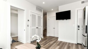 Un appartamento moderno con pavimento in legno, pareti bianche, televisione a schermo piatto, frigorifero e una scala che conduce a un altro livello.