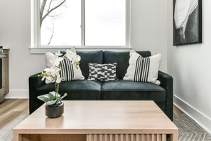 A dark green sofa with three pillows, a wooden coffee table, and a potted orchid.