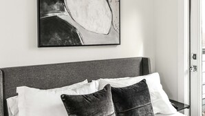 Una camera da letto con un letto, cuscini, una testiera e un quadro astratto appeso al muro.