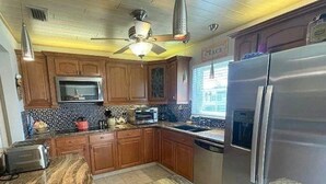 Una cocina con gabinetes de madera, microondas, tostadora, refrigerador y ventilador de techo.
