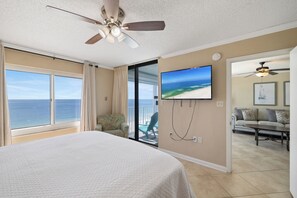 A bedroom with a bed, a ceiling fan, a TV, a balcony with a view of the ocean, and a living area with a sofa and a coffee table. - Summerchase 1003 by Liquid Life (Orange Beach)