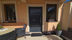 Eine Terrasse mit Tisch, Stühlen und Blumentöpfen sowie einer schwarzen Tür.