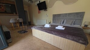 Ein Schlafzimmer mit einem großen Bett, einem an der Wand montierten Fernseher und einem Schreibtisch mit Stühlen.