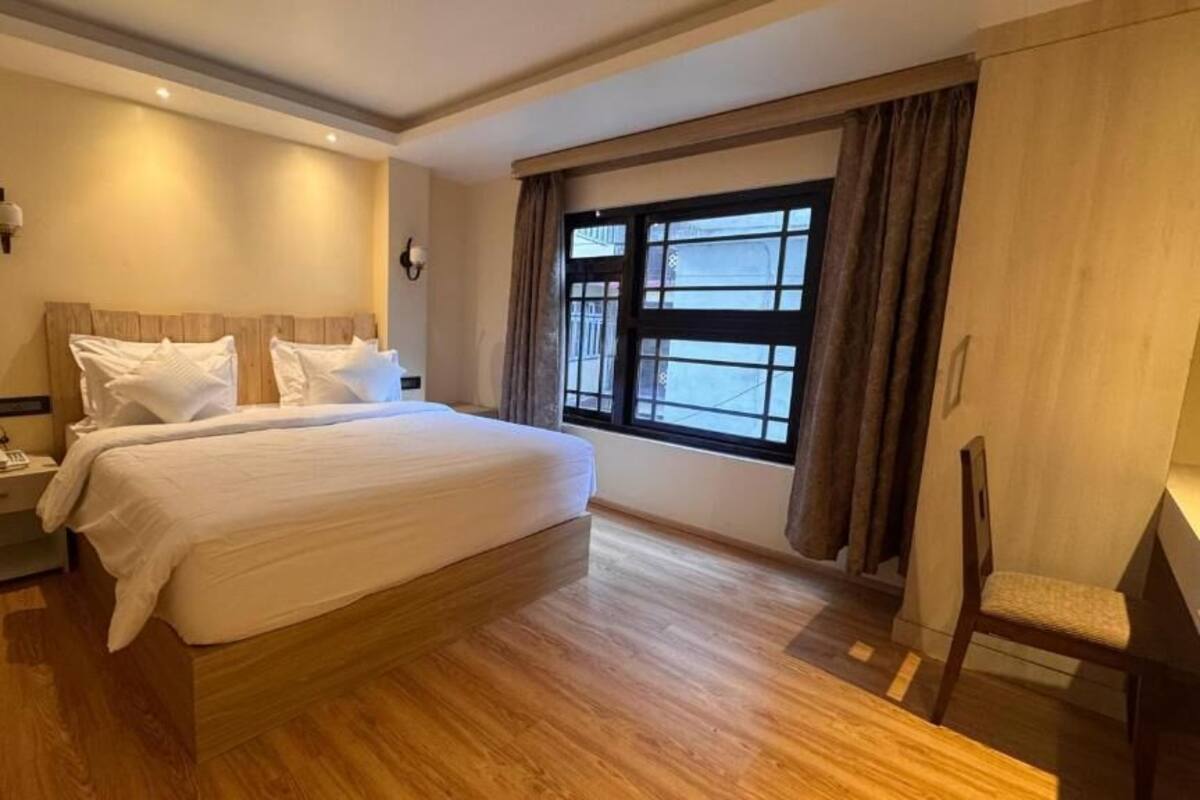 Ein Schlafzimmer mit einem großen Bett, Holzboden, einem Nachttisch, einem Sessel und einem Fenster mit Vorhängen.