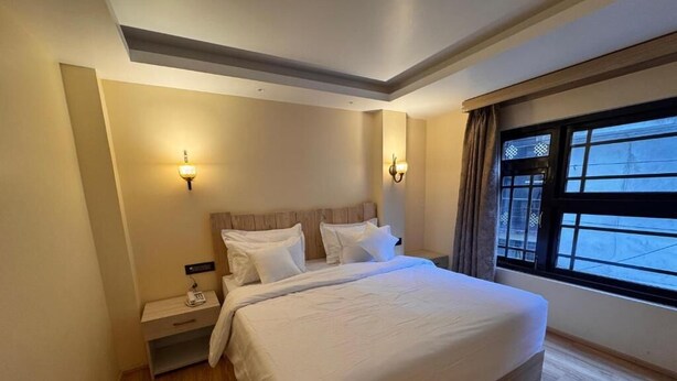 A hotel room with a large bed, bedside tables, wall-mounted lights, and a window with curtains. - Juniper Mountain Resort (Lachen)
