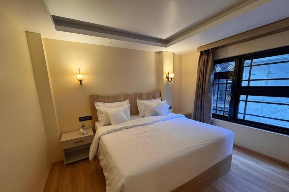 Ein Hotelzimmer mit einem großen Bett, Nachttischen, Wandleuchten und einem fensterbepflanzten Fenster mit Vorhängen.