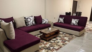 Ein Wohnzimmer mit zwei Sofas, einem Couchtisch, einem gemusterten Teppich und einer Tür im Hintergrund.