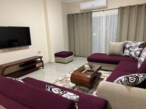 A living room with a flat-screen TV, a wooden entertainment unit, a sofa, a coffee table, and a patterned rug.
