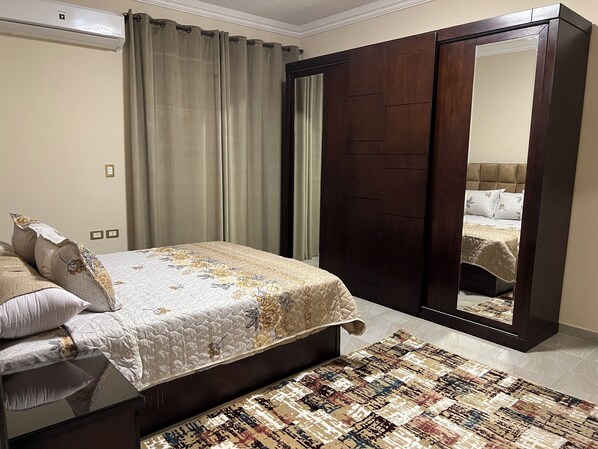 A bedroom with a bed, a large mirror, a wardrobe, and a patterned rug.