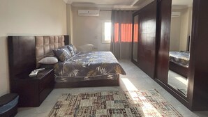 A bedroom with a large bed, a nightstand, a dresser, a mirror, and a window with curtains. - Elite House: Elegant & Spacious 3BR Apartment 2 –  Mall of Arabia (Giza Governorate)