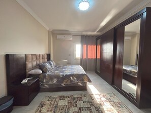 Ein Schlafzimmer mit einem großen Bett, einem Nachttisch, einer Kommode, einem Spiegel und einem Fenster mit Vorhängen.