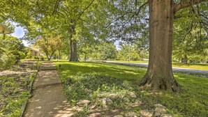 Un chemin bordé d’arbres et délimité par une bordure en pierre, qui mène à un bâtiment dont l’entrée est bien visible.