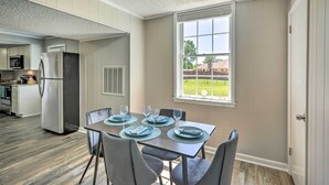 Un coin repas avec une table dressée pour quatre personnes, une cuisine en arrière-plan et une fenêtre donnant sur une cour.