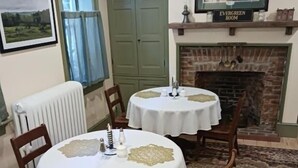 A dining room with two round tables, chairs, a fireplace, a framed picture, and a window with curtains. - Langdon Hill House (Gettysburg)
