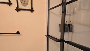 Ein Badezimmer mit Toilette, gerahmten Bildern an der Wand, einem Handtuchhalter und einer Duschkabine aus Glas.