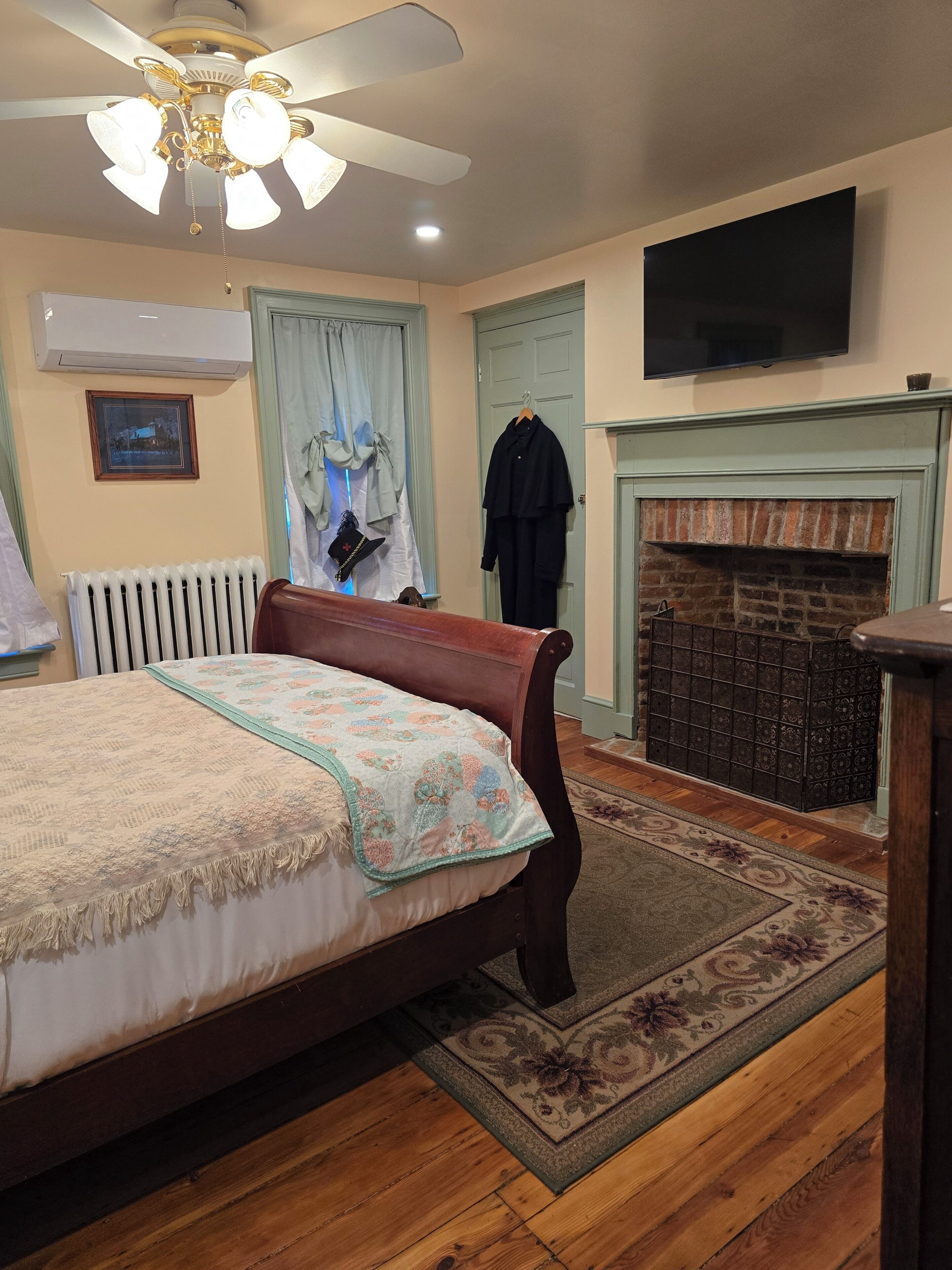 A bedroom with a bed, a ceiling fan, a fireplace, a TV, and a radiator.